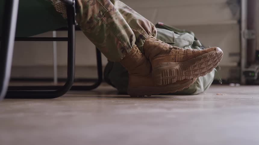 Military boot rests on the floor beside a green backpack