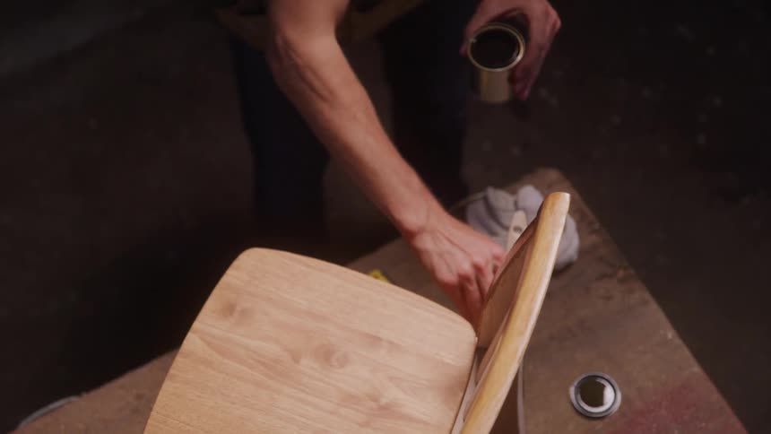 Male carpenter staining a wood chair with a brush