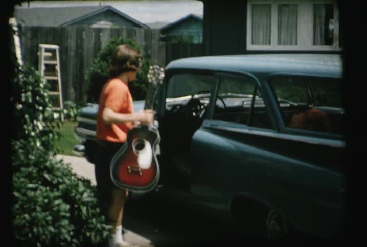 A person picks up a guitar and places it inside a vehicle