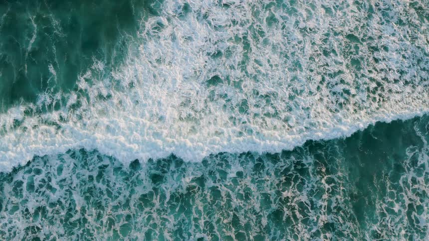 Ocean waves crash forming white foam over the blue surface