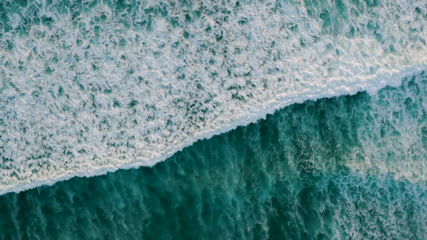 Aerial view of ocean waves breaking with white foam over turquoiseblue water