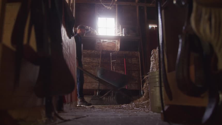 Man is pushing a wheelbarrow through the stables