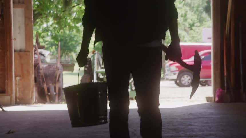 Silhouette of a person with a hoe in a bucket coming out of a shed