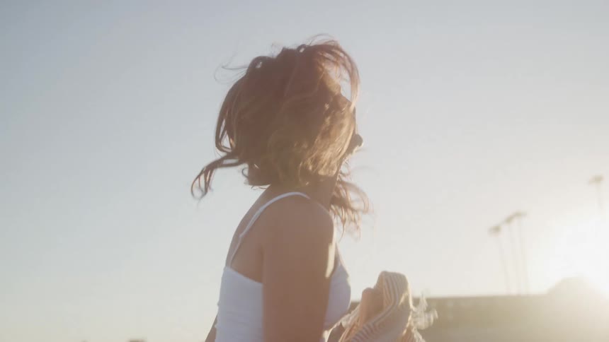 A young woman holds a blanket laughing and walking on the beach having fun at sunset