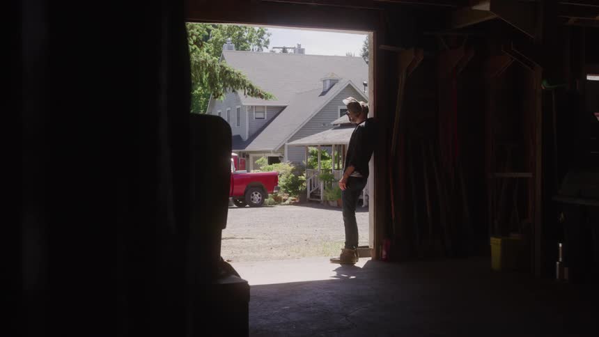Man wearing a cap rubbing his face while standing in the doorway of a warehouse