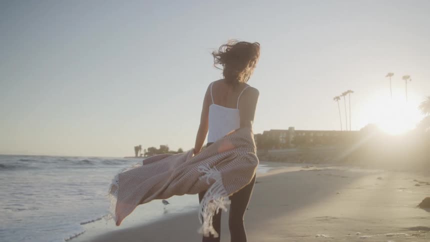 A woman holds a blanket while running on the beach at sunset