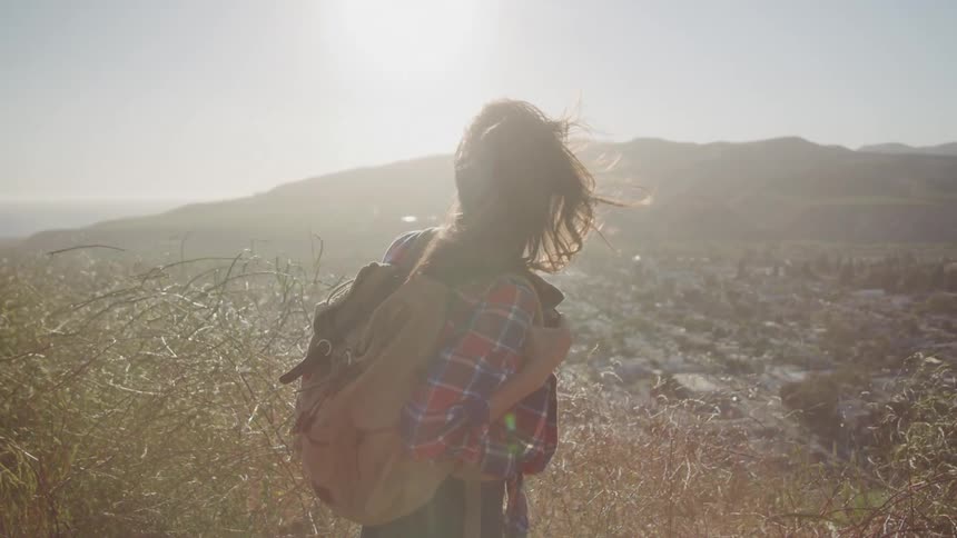 Woman with a backpack on a mountain peak overlooking a city