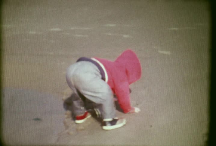 A young child playing in the sand on a beach as the water comes in