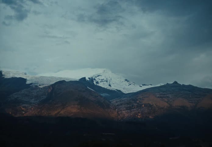 Snowcovered mountain range contrasts with arid slopes beneath a cloudy sky
