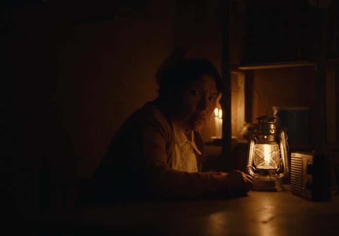 A woman anxiously listens to a radio while sitting at a table indoors at night