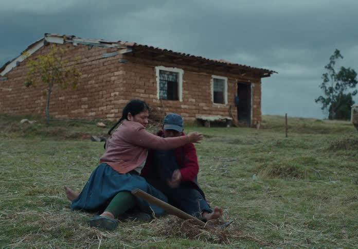 A woman digs in a grassy field as a man stands nearby both stare offframe then suddenly startled he rushes to her and they drop embracing tightly