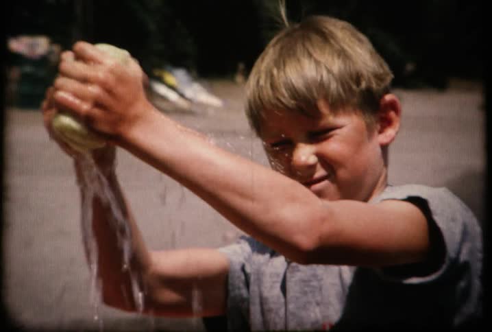 A boy washing a boat near some waterway and wringing out the sponge