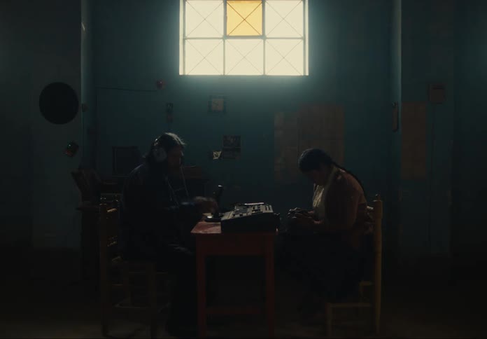 Two people sit face to face in a dark room with a lit window in the background