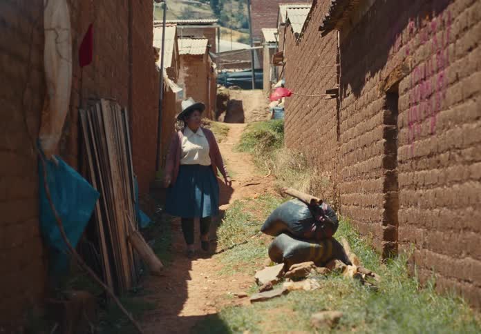 Woman walks through a narrow dirt alley between adobe brick houses in a rural area