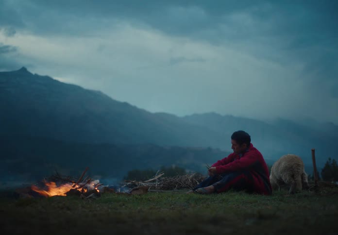 Man sits beside a campfire looking down at dusk in the mountains