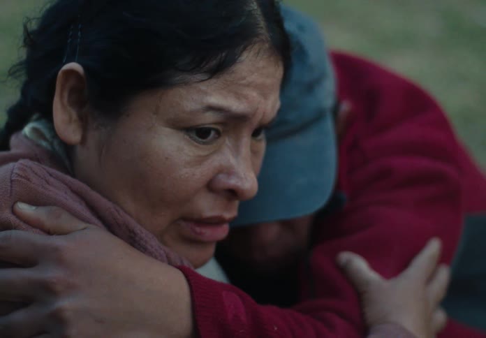 A woman hugs her son outdoors at midday looking fearful