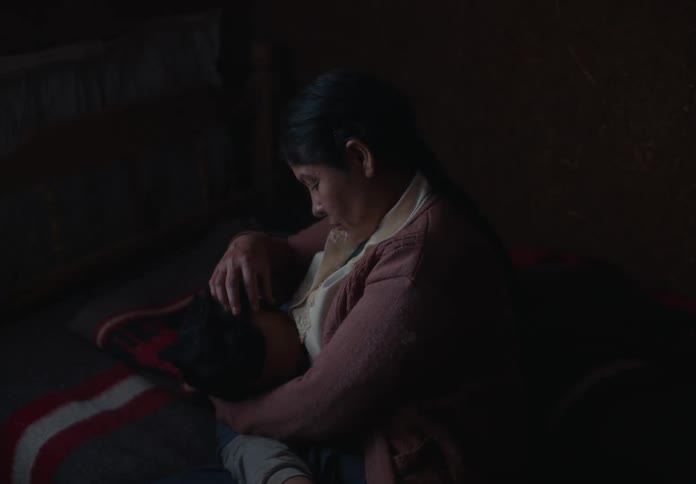 Woman sitting on a bed holds a sleeping child in her arms in a dim and cozy setting