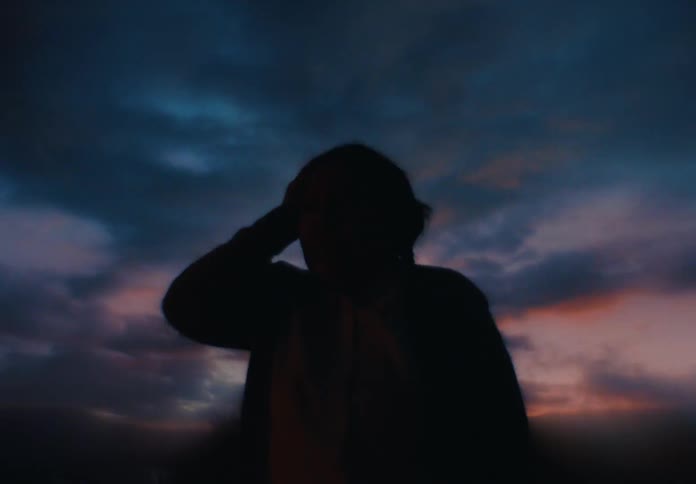 A woman stands silhouetted against a vivid twilight sky with deep blues and soft orange hues