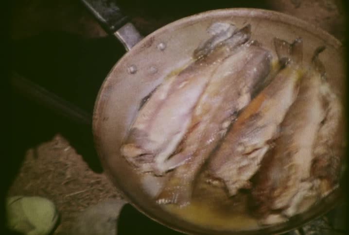 A chef cooks fish in a skillet atop hot coals