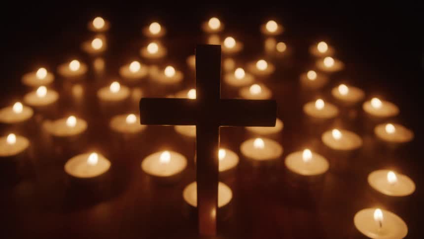 A cross stands in front of several lit candles