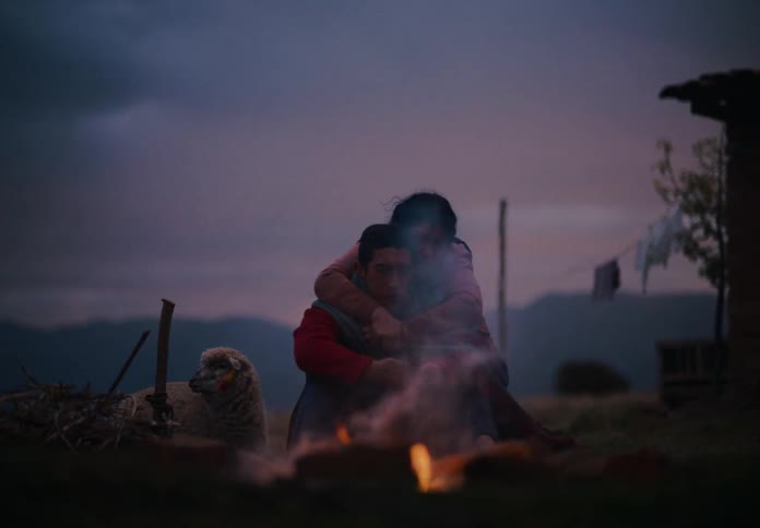 Couple embraces near a campfire at dusk in a rural area