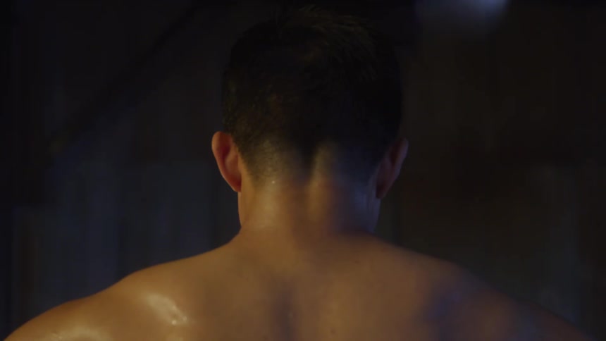 A closeup shot of the back of a shirtless persons head and shoulders with sweat visible on the skin set against a dark and blurry background