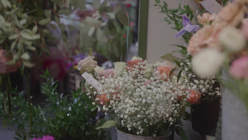 Elderly woman closely observes a flower arrangement in a room decorated with lights