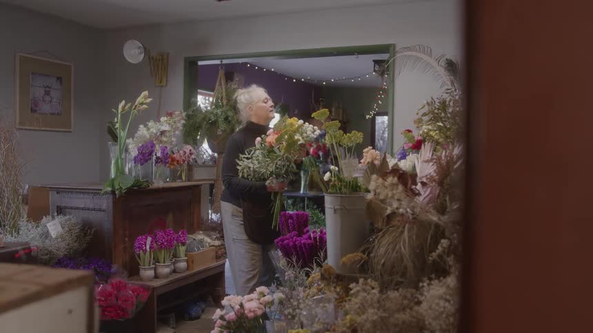 Woman holding colorful bouquets while arranging flowers in a flower shop filled with floral displays