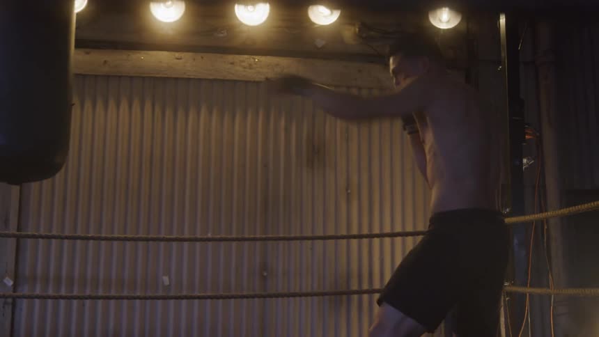 Boxer trains punches on heavy bag inside dimly lit ring
