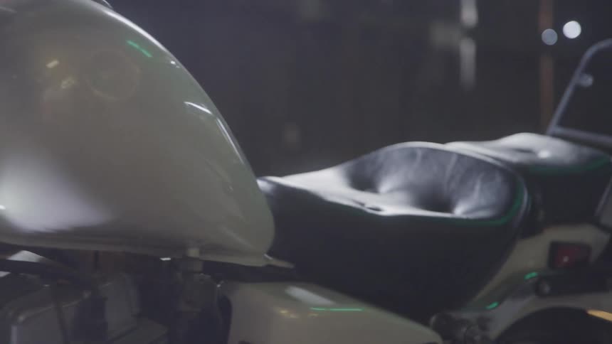 A detailed shot of a parked classic motorcycle shows the front headlight the curved gas tank and the worn leather seat