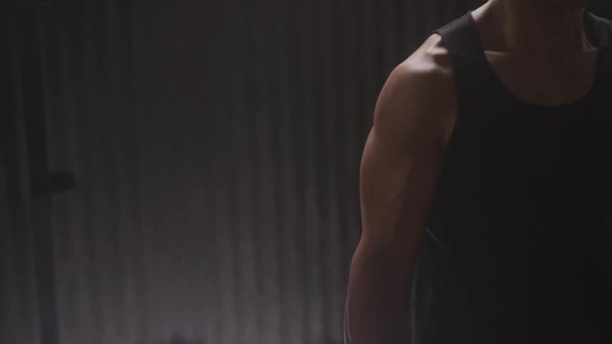 Muscular arm lifts dumbbell during workout in a dimly lit setting
