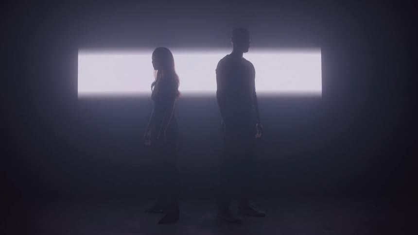 Man and a woman stand back to back in front of a bright panel