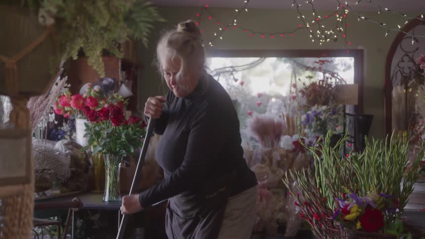 Older woman sweeps the floor of a flower shop decorated