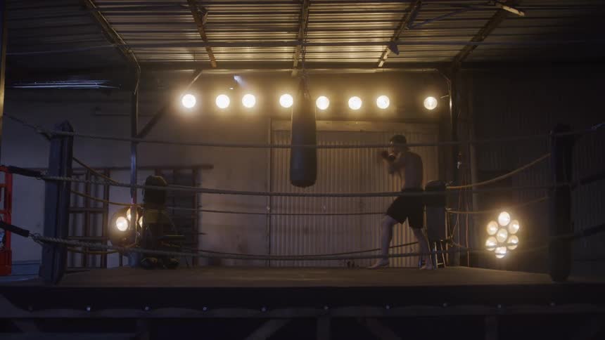 Man gets ready to train in a lit boxing ring inside an industrial warehouse