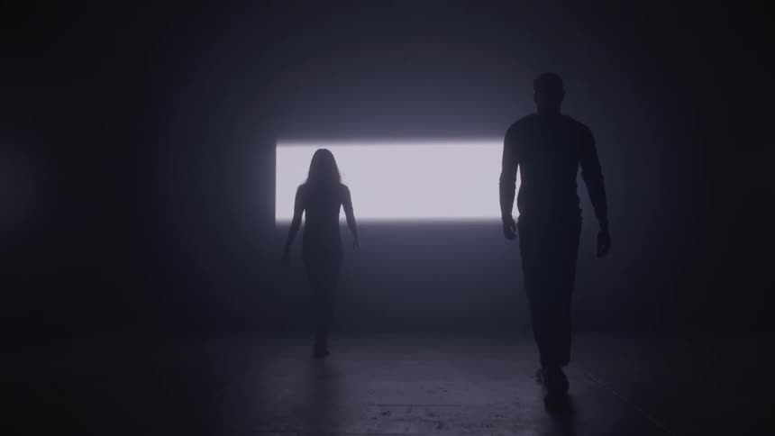Silhouettes of a man and a woman walking toward a bright rectangular light