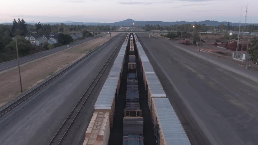 A cargo train runs along tracks in the middle of the road in a rural area at midday