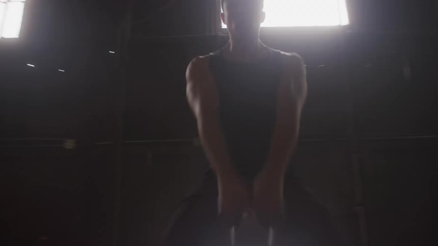 A young asian man exercises with a gym weight in a hall during daytime