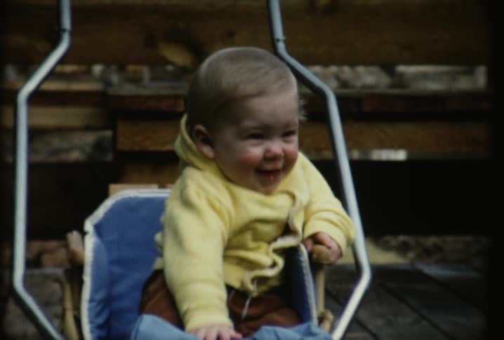 A baby sitting in a swing and laughing and smiling at someone