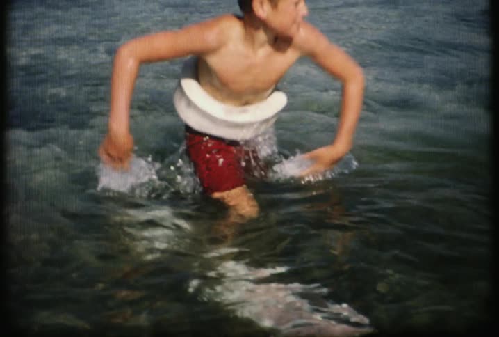 A boy playing in some water with a float around his waist