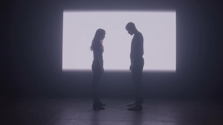 Silhouette of a man and a woman facing each other with light reflected on a wall in the background