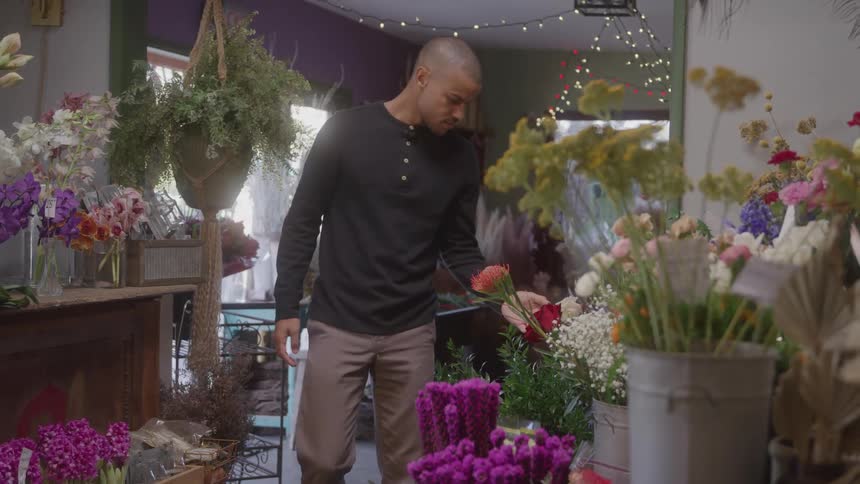 Man walks among colorful floral arrangements in a flower shop decorated with lights