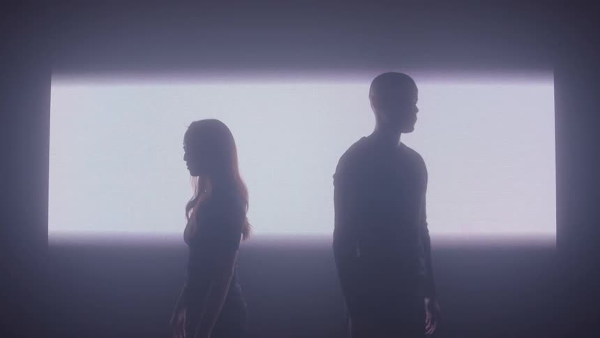 The wall lights up in back of two people in a dark room