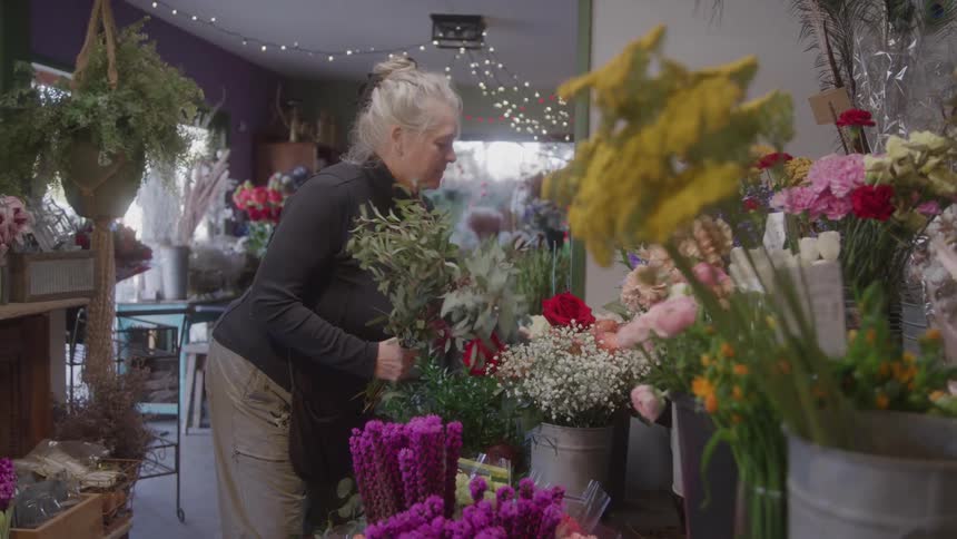 A woman arranges a variety of flowers in a vibrant shop filled with colorful blooms and soft lighting