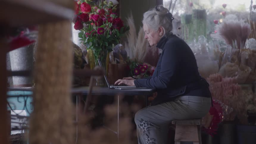 The woman is using a laptop in the flower shop
