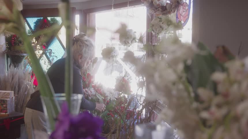 Woman arranging flowers in a bouquet near a sunlit window