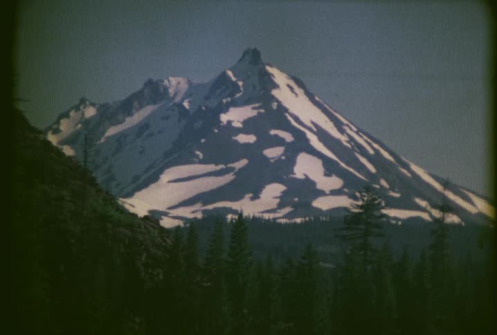 Snow covers a tall mountain in front of a forest