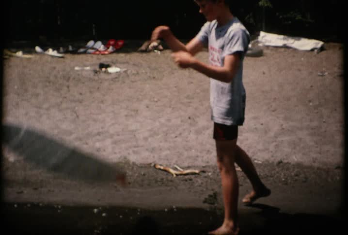 A boy throws a board into the water and starts to take off his shirt