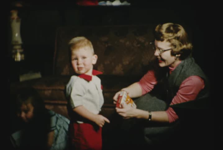 A woman helps a child unwrap a present