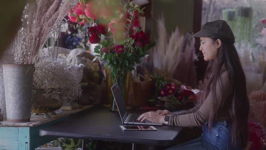 Woman works on a laptop while sitting in a flower shop