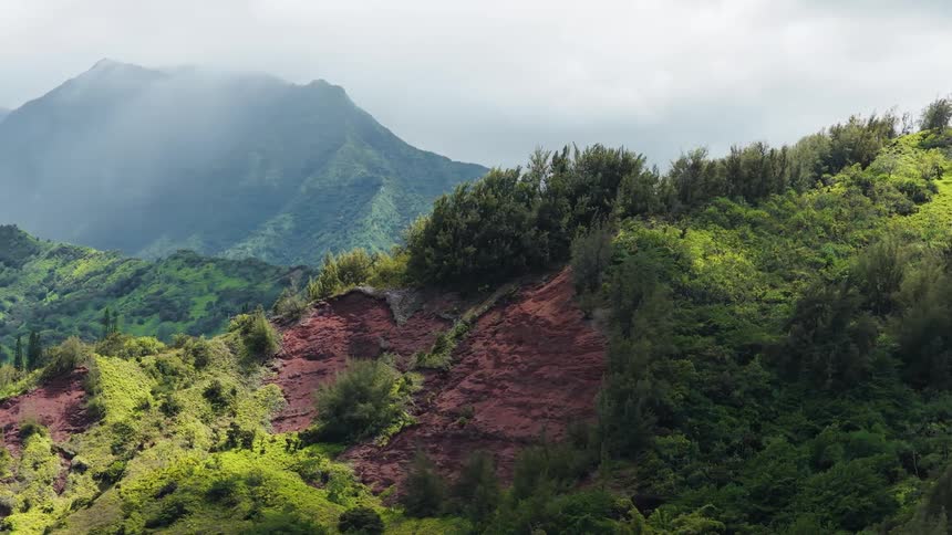 Mountains covered in dense vegetation reveal reddish slopes beneath the mist
